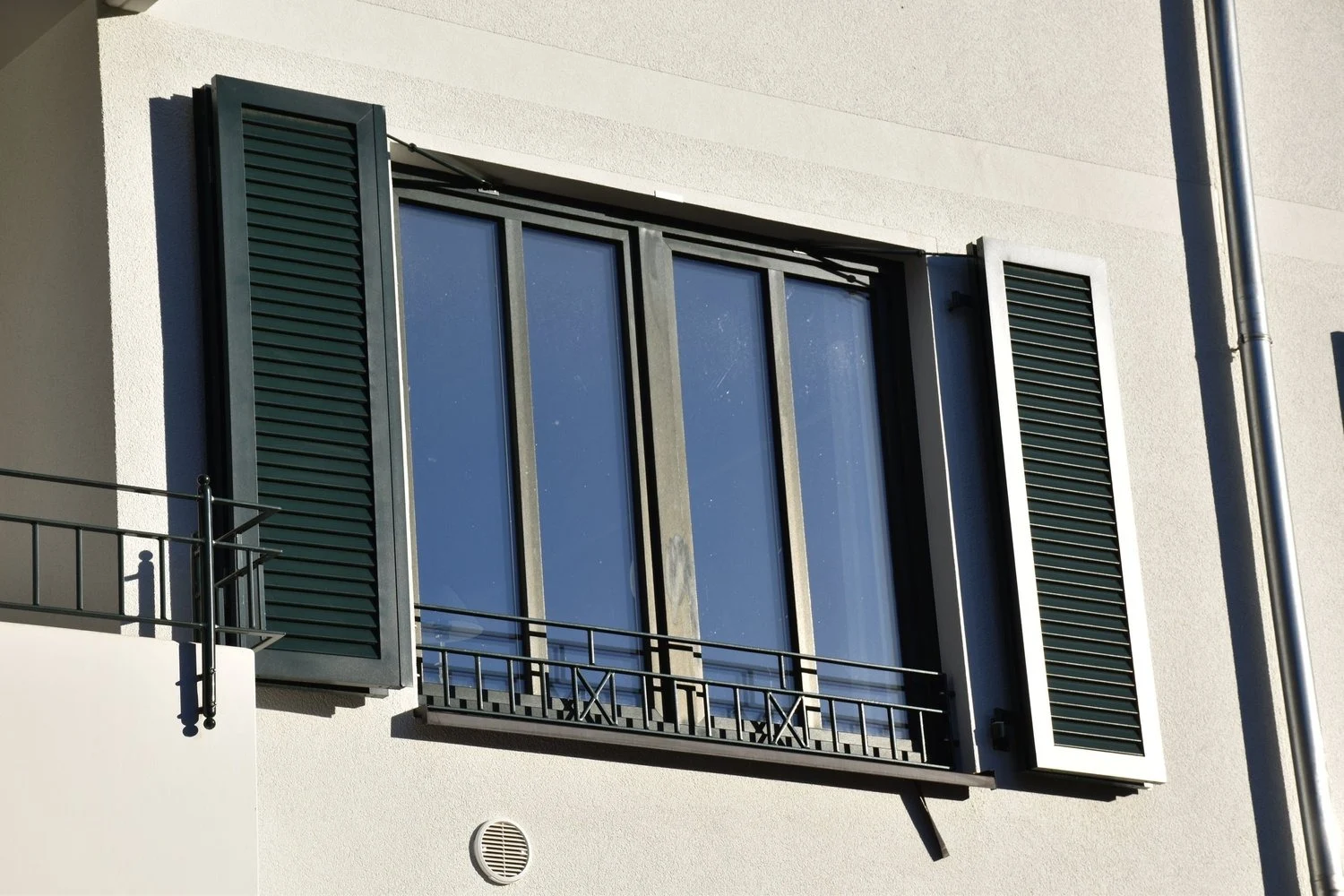 Große Fensteranlage mit dunklen Rahmen und grünen Fensterläden