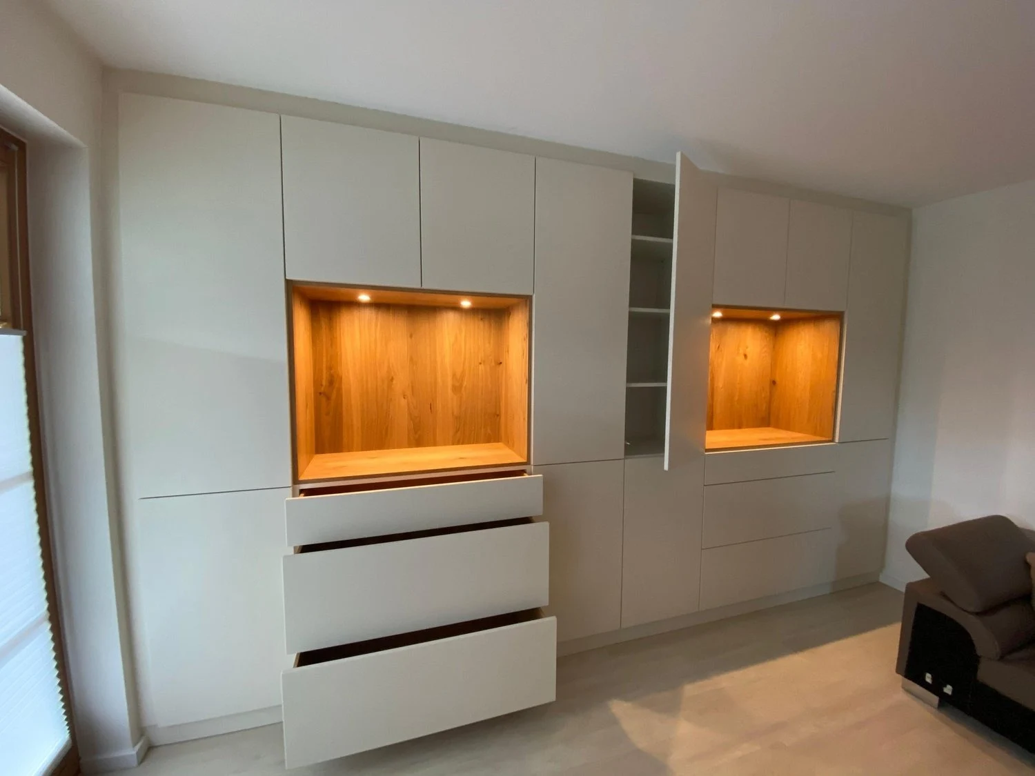 Maßgefertigter Wohnzimmerschrank mit hellen Fronten und beleuchteten Holznischen